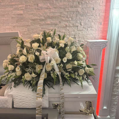White rose funeral casket spray with lilies and ribbon on a casket