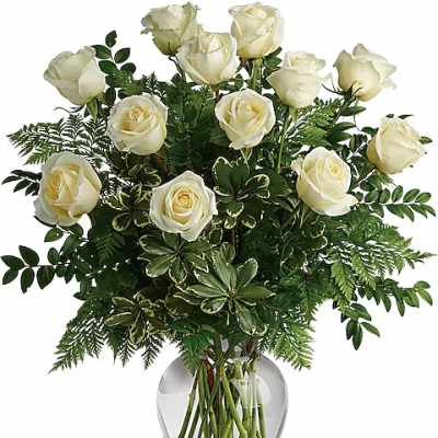 White roses arranged in a clear glass vase with mixed greenery
