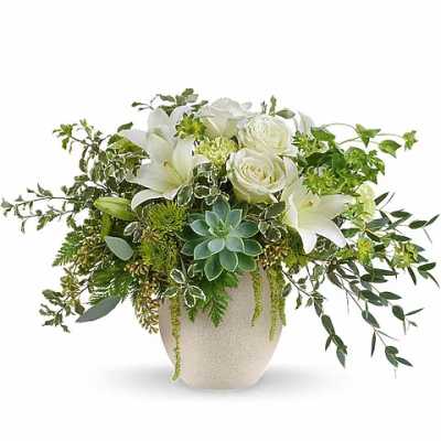 White roses and lilies arranged in a beige vase with trailing greenery