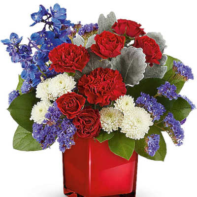 Red roses, white mums, and blue flowers in a red glass vase