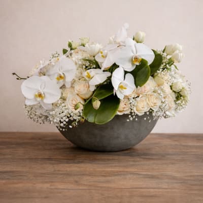 White orchids and cream roses arranged in a low gray bowl