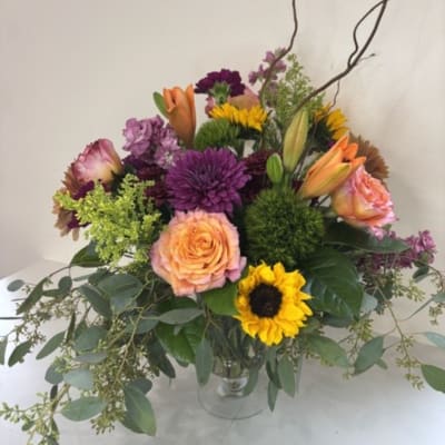 Mixed bouquet of purple, peach, and yellow flowers in a clear vase