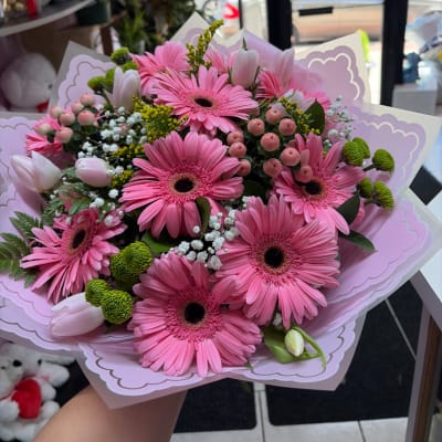 Pink gerbera daisy bouquet with tulips and small filler flowers in pastel wrapping