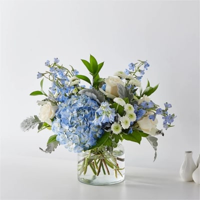 Blue hydrangea and white rose arrangement in a clear glass vase