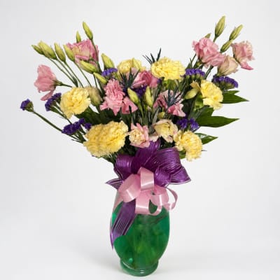 Pink and yellow mixed bouquet in a green glass vase with purple ribbon