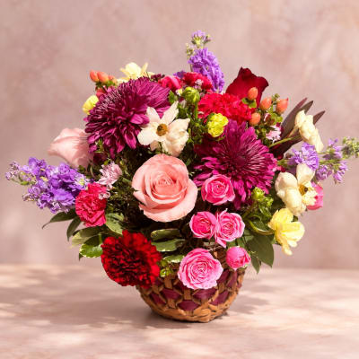 Mixed bouquet in a woven basket with pink, purple, red, and cream flowers