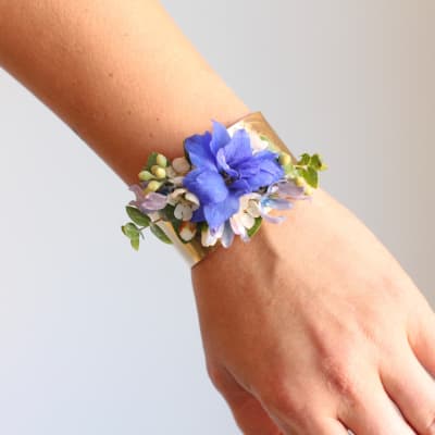Blue floral wrist corsage on a gold cuff bracelet