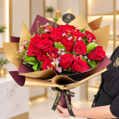 Handheld bouquet of red roses with pink filler flowers in gold and burgundy wrap