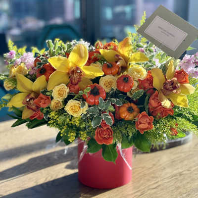 Bright mixed flower arrangement in a pink vase with yellow orchids and roses
