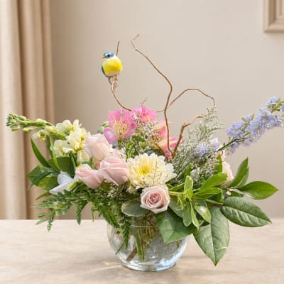 Pastel flower arrangement in a clear glass vase with a small bird ornament