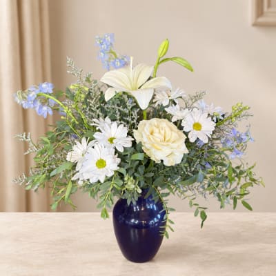 White lilies and daisies in a dark blue vase with blue accents