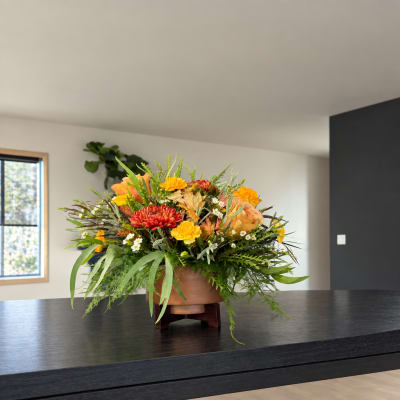 Mixed orange, yellow, and red flowers arranged in a low bowl on a stand