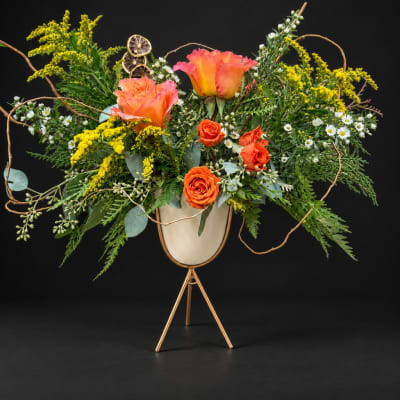 Orange roses and yellow flowers in a gold stand vase