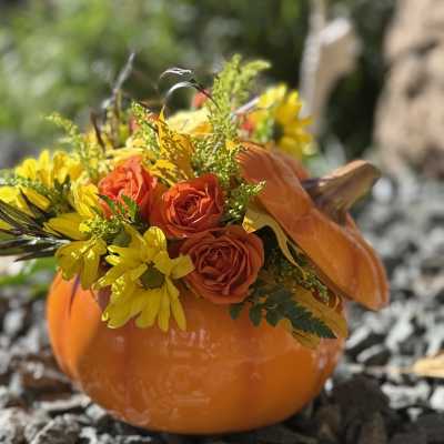 Orange pumpkin container filled with orange roses and yellow daisies