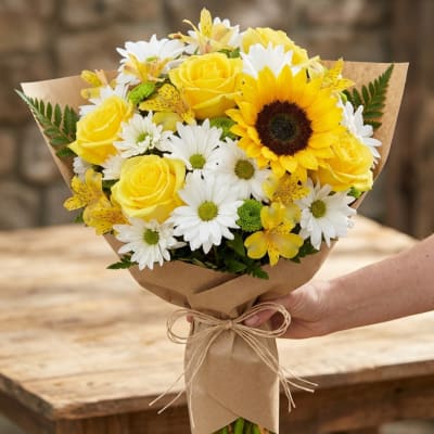 Bouquet of yellow roses, white daisies, and a sunflower wrapped in kraft paper