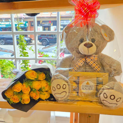 Yellow rose bouquet beside a teddy bear and Ferrero Rocher chocolates