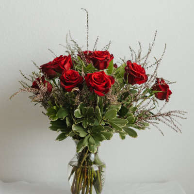Red roses arranged in a clear glass vase with greenery