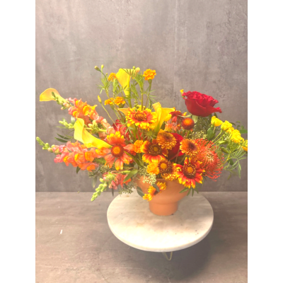 Bright mixed flower arrangement in a peach vase with red and yellow blooms