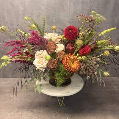 Large mixed floral arrangement in a dark vase with cream, red, and orange blooms