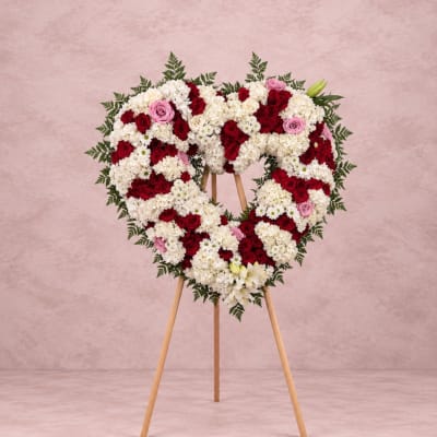 Heart-shaped floral wreath on a wooden easel with red, white, and pink flowers