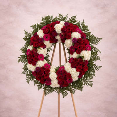 Circular floral wreath on a wooden easel with red, white, and pink flowers