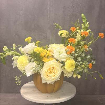 Yellow and white floral arrangement in a pumpkin-shaped vase
