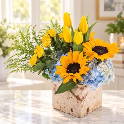 Sunflowers, yellow tulips, roses, and blue hydrangeas in a birch box