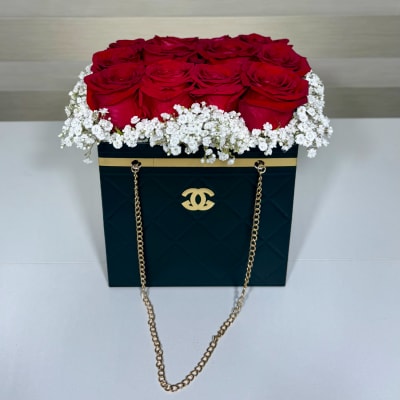 Red roses arranged in a black box with white baby's breath and gold chain handles.