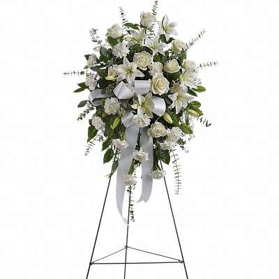 Tall white standing spray of lilies, roses, and carnations on a metal easel with white ribbon
