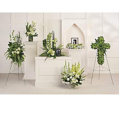 Set of white and green funeral arrangements with standing sprays, cross, and urn display in a chapel.