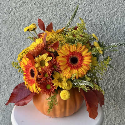 Autumn floral arrangement in a pumpkin-shaped container with orange and yellow blooms