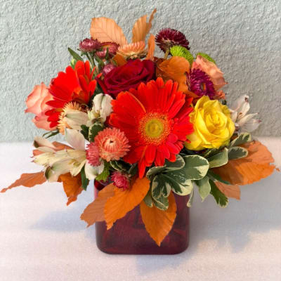 Mixed bouquet in a burgundy vase with red, yellow, and peach flowers