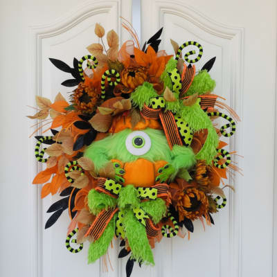Halloween wreath with a green one-eyed monster face and orange accents