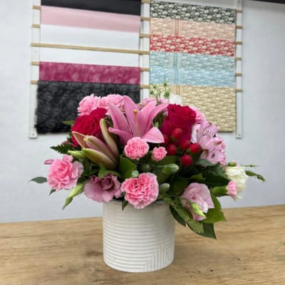 Pink lilies, roses, and carnations arranged in a white vase