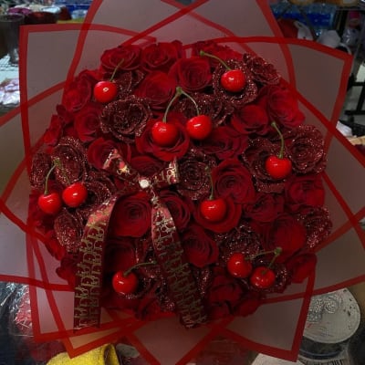 Round bouquet of red roses with decorative cherries and ribbon