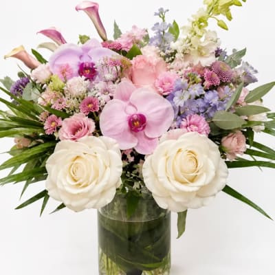 Pastel mixed flower arrangement in a clear glass vase with orchids and roses