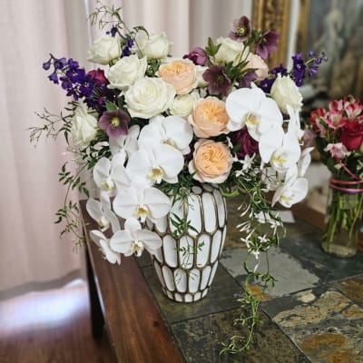 White orchids and roses in a decorative vase with purple accents