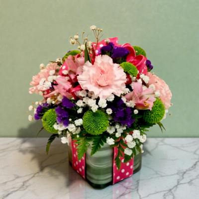 Mixed pink, purple, and green flower arrangement in a glass vase with a pink ribbon