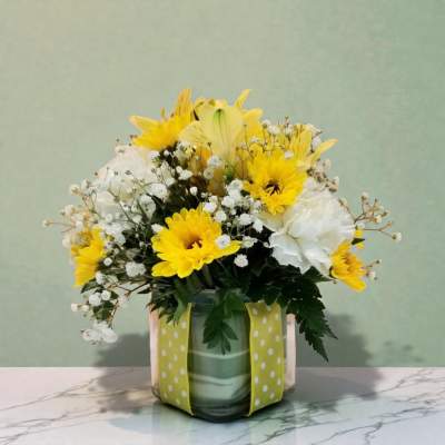 Yellow and white flower arrangement in a glass vase with a polka-dot ribbon