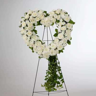 Heart-shaped white rose wreath on a stand with trailing greenery