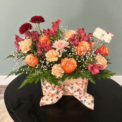 Mixed bouquet of orange and pink flowers in a floral box with a ribbon