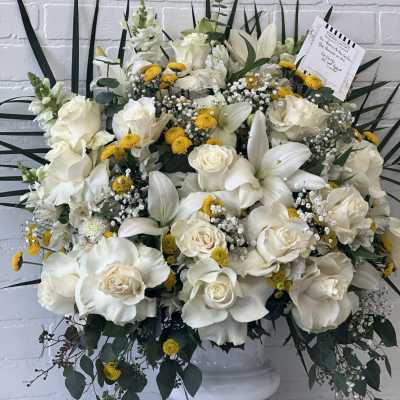 White roses and lilies in a white pedestal vase with yellow accents