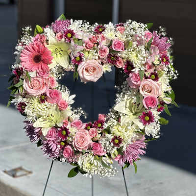 Heart-shaped floral wreath with pink roses and white lilies on a stand