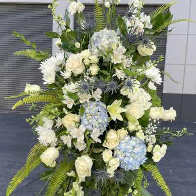 Tall white floral standing spray with blue hydrangeas and greenery
