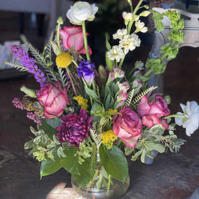 Mixed bouquet of pink roses, white blooms, and purple flowers in a glass vase