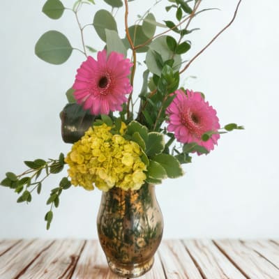 Pink gerbera daisies and yellow hydrangea in a glass vase