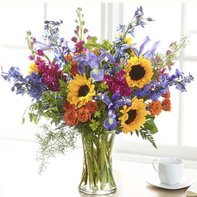 Mixed bouquet of sunflowers, irises, and orange roses in a glass vase