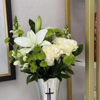 White lilies and roses in a silver vase with a cross