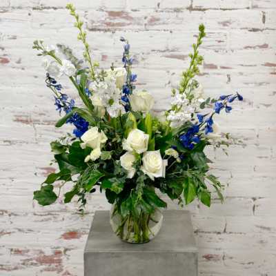 White roses and blue flowers arranged in a clear glass vase