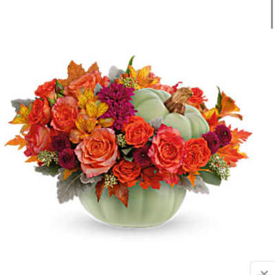 Autumn bouquet of orange roses and mixed flowers in a pale green pumpkin vase